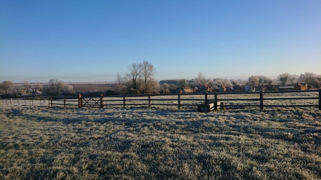 Icy landscape with fence and bare trees in the distance and a blue sky